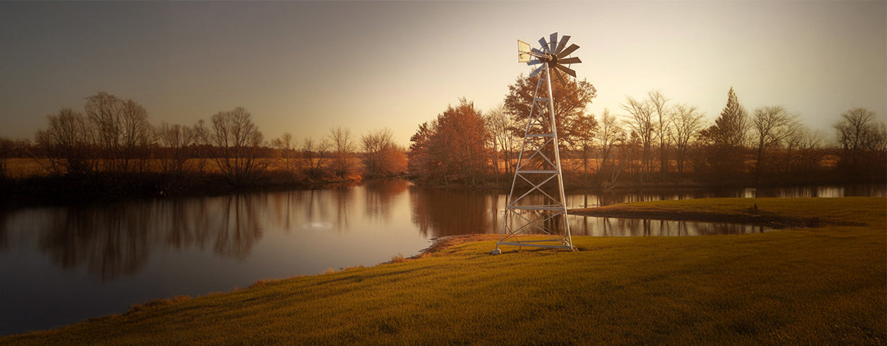Windmill by a lake at sunset, rural landscape photography.