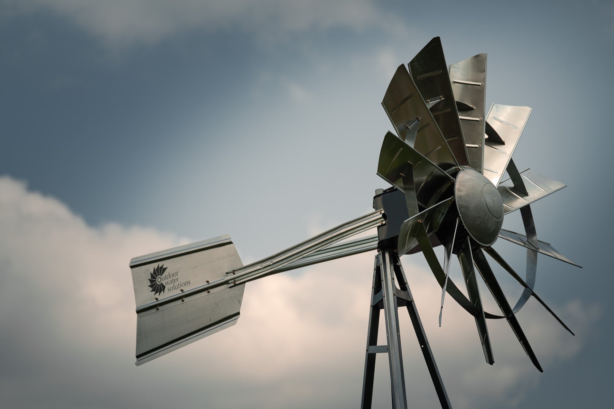 Close-up of an Outdoor Water Solutions galvanized steel aeration windmill against a cloudy sky.