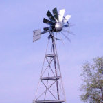 Close up of a silver 3-legged windmill head against a blue sky.