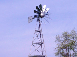Close up of a silver 3-legged windmill head against a blue sky.