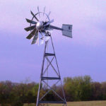 A silver 3-legged windmill against a blue sky.