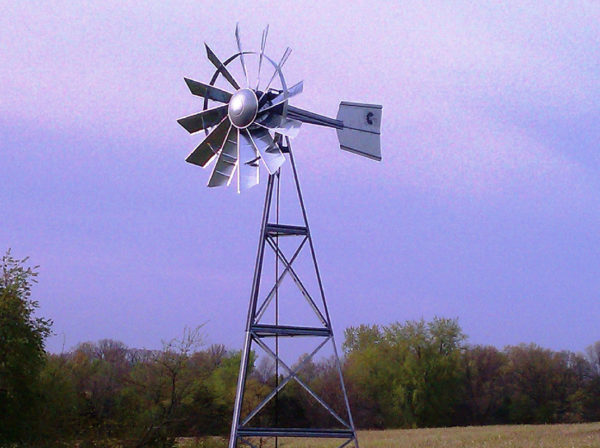A silver 3-legged windmill against a blue sky.