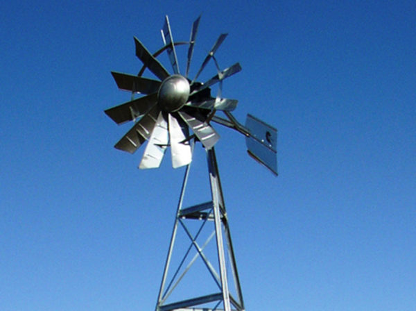 A silver windmill including the top of the windmill frame on a blue sky background.