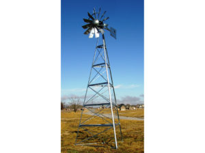 A silver windmill in a field with a sky, grass and houses around it.