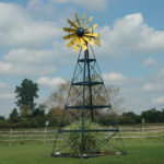 A 4-legged windmill with a yellow windmill head against a background of sky and grass.