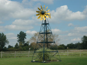 A 4-legged windmill with a yellow windmill head against a background of sky and grass.