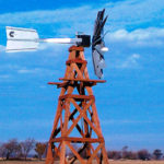 A silver windmill head on a wooden windmill. There is a blue sky in the background.
