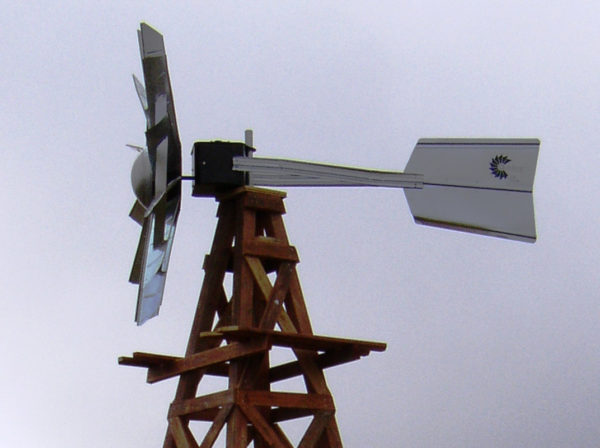 A silver windmill head on a wooden windmill. There is a blue sky in the background.