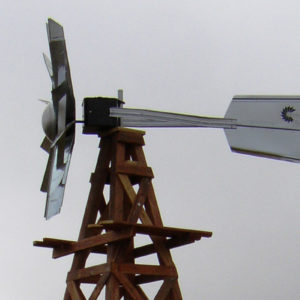 A silver windmill head on a wooden windmill. There is a blue sky in the background.