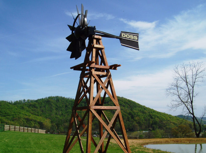 Windmill head and tail on a wooden windmill tower. The head and tail are black. The background is a blue sky with light clouds and green grass with a hill.