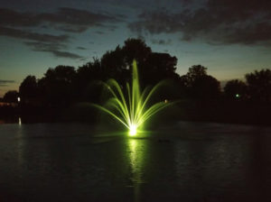 A single floating fountain lit up with LED lights creating a brilliant light display at night.