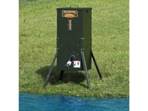 A 70 pound Texas Hunter Fish Feeder on a shore of a pond.