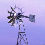 A silver 3-legged windmill against a blue sky.