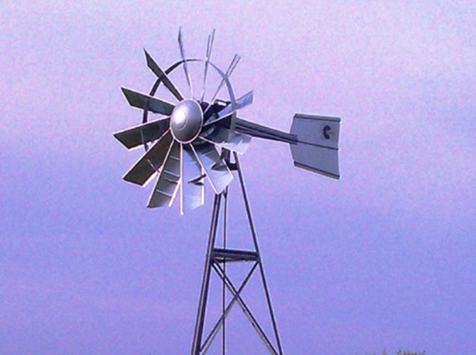A silver 3-legged windmill against a blue sky.