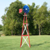 A blue, red, and white Small Backyard Windmill on grass with trees in the background.