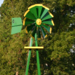 Close up of a green and yellow Small Backyard Windmill on grass with trees in the background.