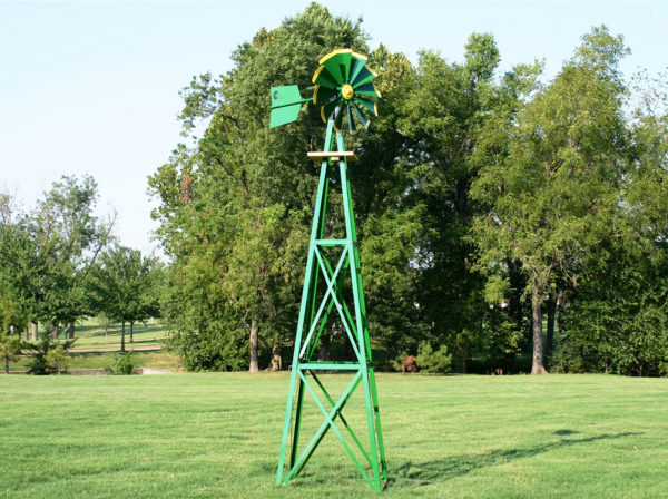 A green and yellow Small Backyard Windmill on grass with trees in the background.