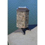 A camo fish feeder with a small solar panel on top at the end of a dock.