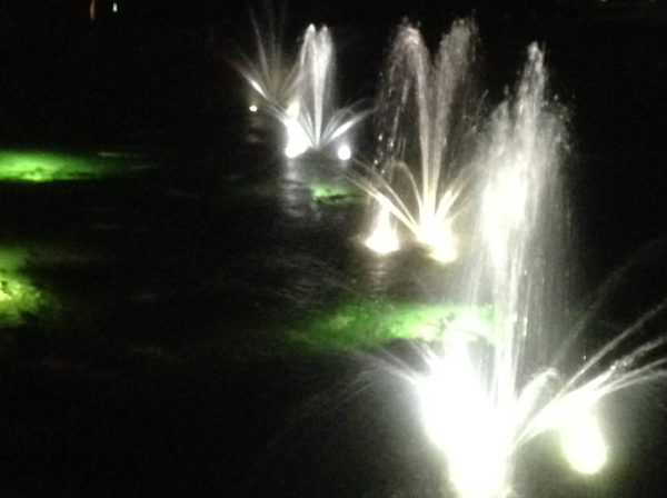 Several floating pond fountains at night. It is lit up with LEDs so the water is visible in the dark.