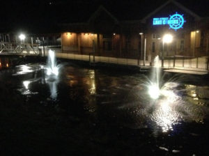 Several floating pond fountains in front of a dock at night.