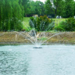 A floating pond fountain at night. It is lit up with LEDs so the water is visible in the dark.