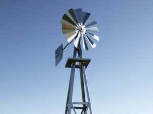 Close up of a silver 3-legged windmill head against a blue sky.