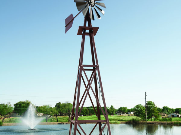 Full image of a Large Backyard Windmill in bronze with trees and a floating fountain in the background.