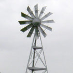 A silver 3-legged windmill against a blue sky.