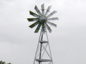 A silver 3-legged windmill against a blue sky.