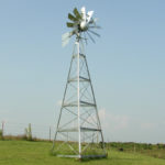 A silver 3-legged windmill against a blue sky.