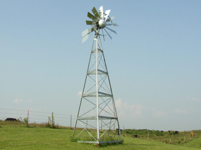 A silver 3-legged windmill against a blue sky.