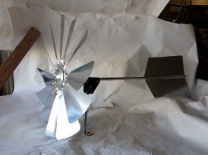 A silver windmill head and tail fin on a white paper background.