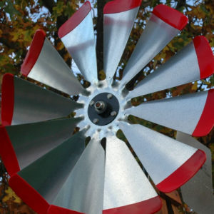 Close up on windmill head in silver with red tips on a wooden windmill body. In the background there are trees.