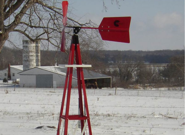 A small, red, backyard windmill in a snowy field.