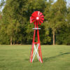 A red and white Small Backyard Windmill on grass with trees in the background.