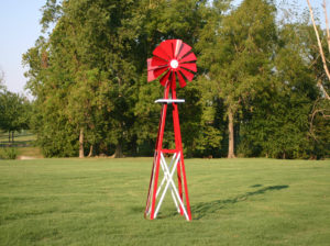A red and white Small Backyard Windmill on grass with trees in the background.
