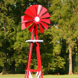 Close up of a red and white Small Backyard Windmill on grass with trees in the background.