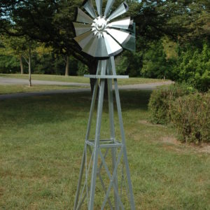 Small silver windmill with black tips. The background is trees.