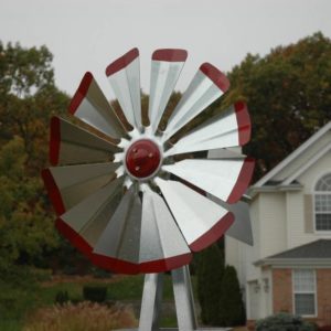 Close up on windmill head in silver with red tips. In the background are trees and a house.