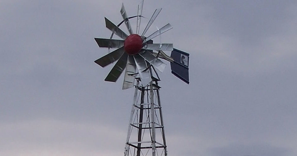 Silver windmill top with a red nose cone. The background is a muted blue sky with clouds.