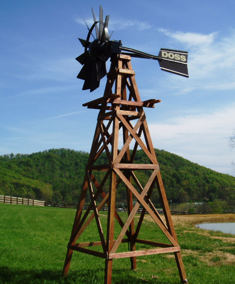 Windmill head and tail on a wooden windmill tower. The head and tail are black. The background is a blue sky with light clouds and green grass with a hill.